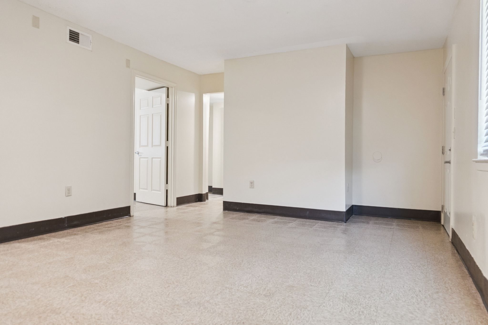 A large empty room with a door on the left and a window on the right.